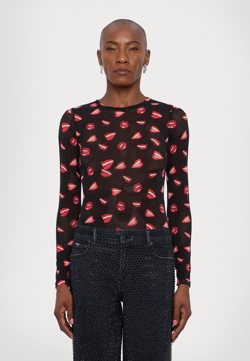 Blusa de manga larga transparente con patrones de bocas rojas sobre fondo negro, combinada con jeans negros con detalles de tachuelas.