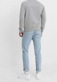 Felpa grigia con orlo a coste, abbinata a jeans azzurri e sneaker bianche. I jeans hanno un orlo risvoltato e tasche posteriori.