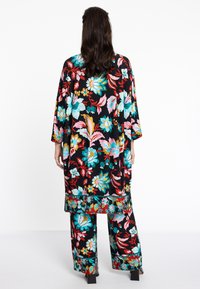 Florale zwarte tuniek en bijpassende broek gemaakt van lichtgewicht stof, met kleurrijke bloesems in roze, blauw en rood, en brede mouwen.