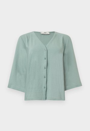 Blouse courte vert clair à col en V avec manches trois-quarts et cinq boutons sur le devant, présentée sur un fond blanc uni.