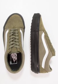 Baskets Vans vert olive avec des rayures blanches sur les côtés, des semelles épaisses en caoutchouc noir texturé et des lacets à l'avant, vues de dessus et de côté.