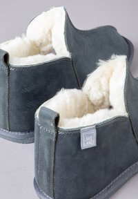 Gray, leather slippers with a soft, cream-colored fur lining. Features a small tag labeled "LAKELAND" and a sturdy sole with stitching details.