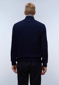 Granatowy sweter dzianinowy z wysokim kołnierzem, posiadający szare wykończenie wewnętrzne i ściągacze na mankietach. Prosty fason, brak widocznych wzorów lub grafik.