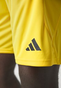 Pantalones cortos deportivos amarillos hechos de una tela suave y ligera. Presenta un logo negro de Adidas en el muslo y detalles de dobladillo cosidos.