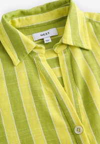 Camicia a righe verde e gialla realizzata in tessuto leggero. Presenta un colletto, chiusura con bottoni e accenti bianchi.