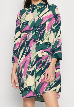 Robe à manches longues avec col, ornée d'un motif abstrait de coups de pinceau et de tourbillons verts, roses, crème et bleu marine, portée par une personne debout.