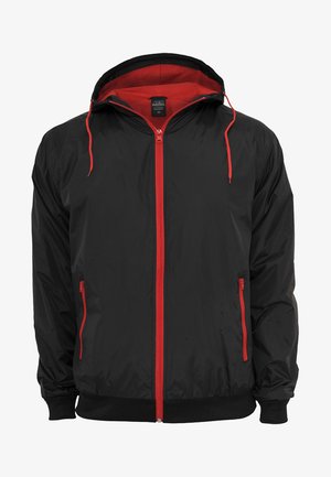 Zwarte jas met een rode binnenvoering en rits. Beschikt over een rode rits en trekkoorden, twee zijzakken met ritsen en geribbelde manchetten.
