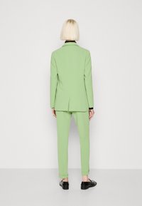 Mint vihreä puku, jossa on muotoiltu design, ei-leveä lapel-takki ja slim-fit housut, yhdistettynä mustiin kenkiin. Sujuva pinta.
