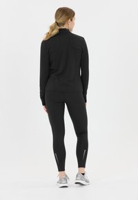 Sort athletic langærmet top med høj krave, parret med sorte leggings med teksturerede paneler, båret med sølvfarvede sneakers.