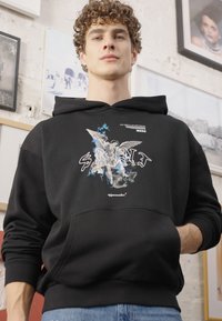 Sudadera negra con un diseño gráfico de ángeles y acentos azules. Fabricada en un tejido suave, con un bolsillo frontal y capucha ajustable con cordón.