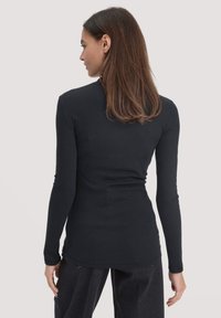 Zwarte long sleeve top met een getailleerd ontwerp. Soepele textuur, ronde hals en gebogen onderrand. Gedragen met een relaxed-fit donker broek.