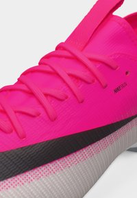Zapato deportivo de color rosa brillante con cordones texturizados, logo negro de swoosh y "NIKESKIN" impreso en el lateral cerca de la suela.