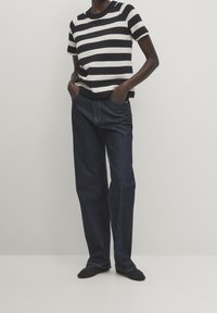 Black and white striped short-sleeve top paired with dark blue loose-fit jeans. The socks are black. Texture is smooth, and denim is sturdy.