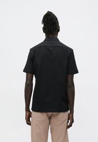 Zwart T-shirt met korte mouwen en geribbelde structuur, voorzien van een kraag en normale pasvorm. Gecombineerd met beige geribbelde broek.