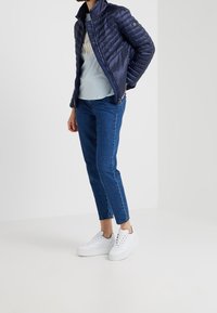 Navy puffer jacket with quilted texture, paired with a light blue T-shirt, blue jeans, and white sneakers. Design features a stand collar.