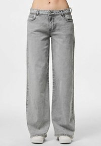 Široke traperice u svijetlosivom denimu, s klasičnom elastičnom trakom, prednjim džepovima i suptilnom izblijedjelom teksturom, te ravnim, opuštenim krojem.