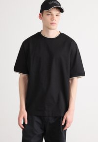 Camiseta negra de manga corta con cuello redondo, que presenta un ribete en contraste en el cuello y las mangas, hecha de suave tejido de algodón.