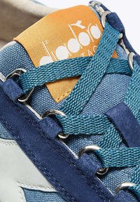Sneakers testurizzati blu e navy con logo arancione. Le caratteristiche includono lacci intrecciati color teal, inserti in suede e occhielli metallici per il fissaggio dei lacci.