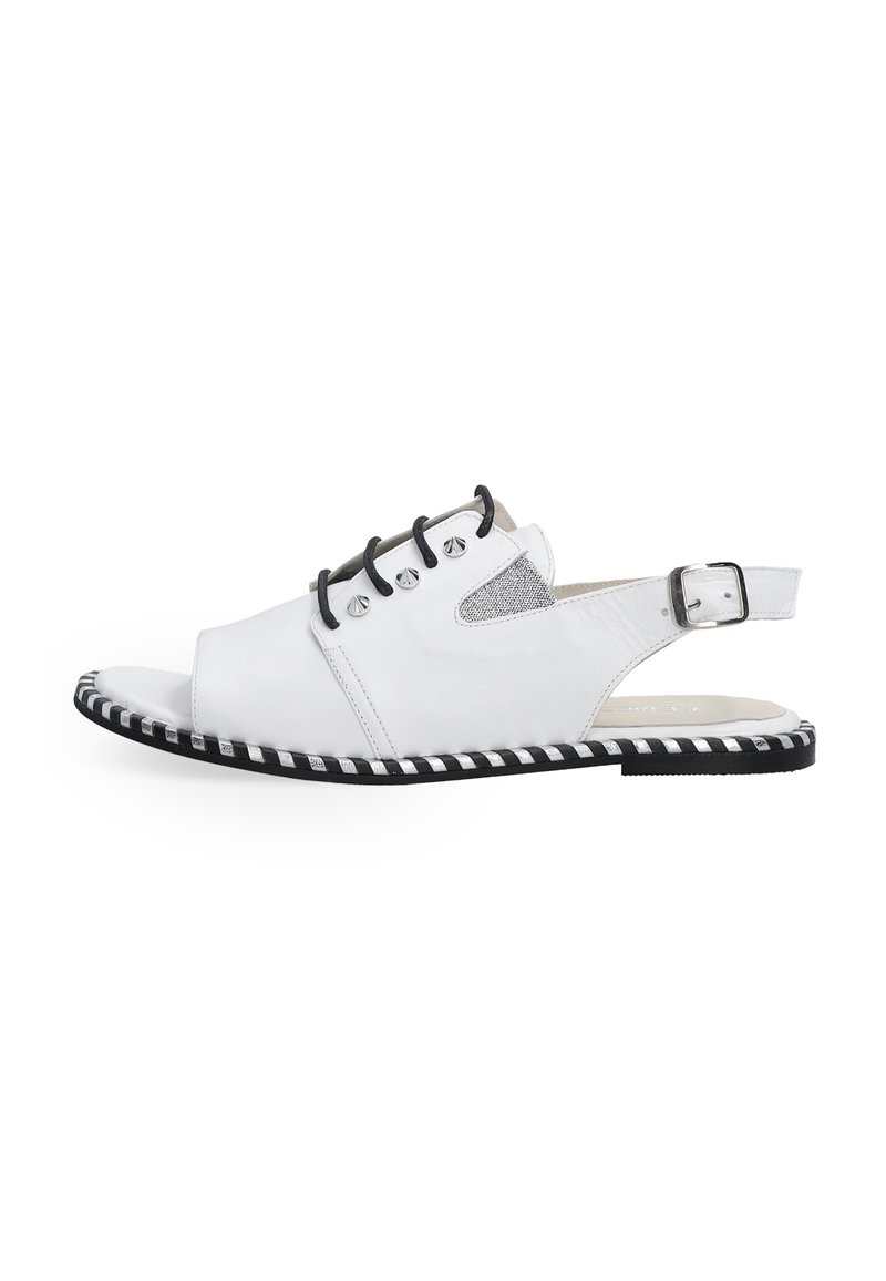 Hvide læderslippers med åben tå, sorte accenter, metaløjer og en stribet sort-hvid sål. Tekstureret sideskæring er synlig.