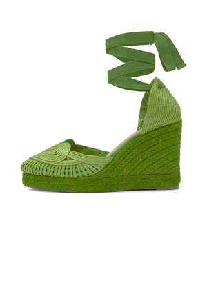 Alpargata cuña verde con textura trenzada, punta cerrada y tiras para atar alrededor del tobillo.