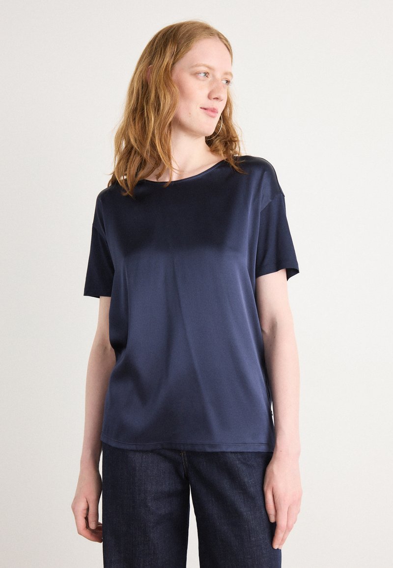 Top blu navy a maniche corte in un materiale liscio e lucido, con scollatura rotonda e vestibilità comoda, abbinato a pantaloni in denim scuro.