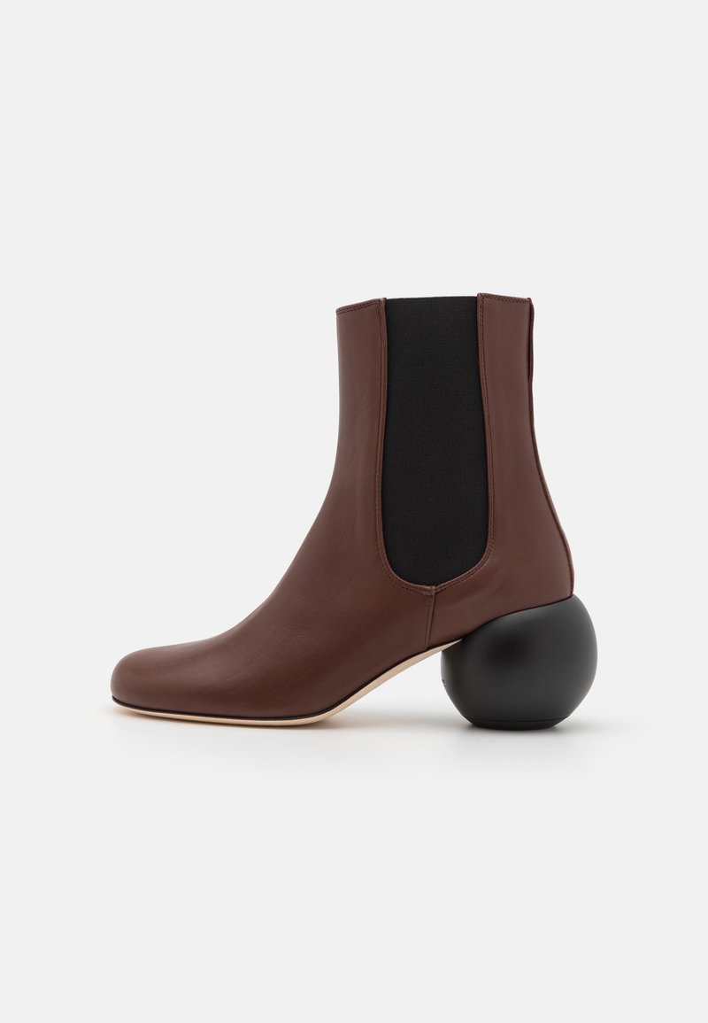 Bottillon en cuir marron avec un talon noir rond, des panneaux latéraux élastiques et un design à bout pointu. Texture lisse et style minimaliste.