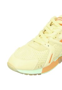 Helles gelbes Sportsneaker mit Obermaterial aus Mesh und Leder, featuring strukturierten Paneelen, dünnen Schnürsenkeln und kontrastierenden orangefarbenen Akzenten an den Seiten.