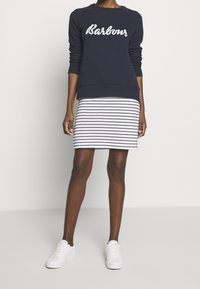 Námořnický svetr s nápisem "Barbour", zkombinovaný s bílou a námořnickou pruhovanou sukní. Nosit s bílými teniskami. Hladká tkanina, ležérní styl.