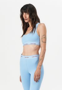 Šviesiai mėlynas sportinis trumpas viršus ir leggingai su Calvin Klein logotipo juosta. Lygi tekstūra, prigludęs dizainas ir minimalistiškas stilius.