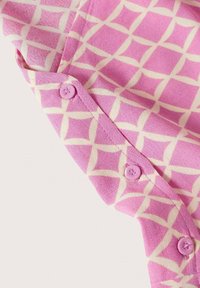 Tissu rose avec un motif géométrique agrémenté d'accents crème. L'image montre un gros plan des boutons et de la texture du tissu.