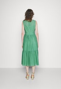Vestido midi verde sin mangas con recortes circulares, tela texturizada y dobladillo en capas. Cuenta con una cintura ajustada y cierre de botones en la parte posterior.