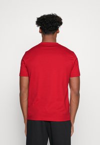 T-shirt rossa in cotone con colletto tondo e maniche corte, texture liscia, design aderente e schiena semplice senza loghi o fantasie visibili.