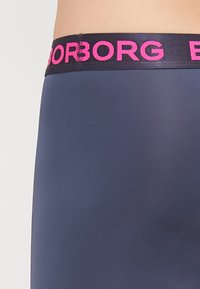 Ναυτικές ελαστικές βερμούδες με φαρδύ μαύρο λάστιχο που έχει έντονα ροζ γράμματα. Το ύφασμα είναι λείο και ελαφρώς ανακλαστικό.