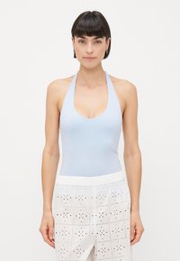 Svijetloplavi bodysuit s halter izrezom i dubokim scoop izrezom, uparen s bijelim hlačama od čipke s cvjetnim izrezima.