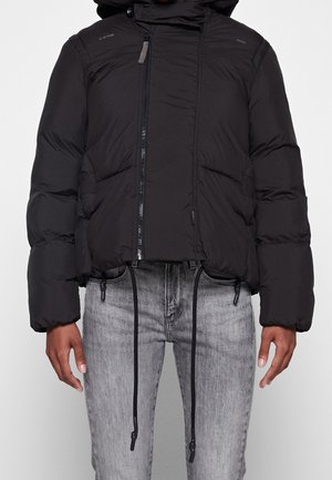 Schwarze gepolsterte Jacke mit Frontreißverschluss, verstellbaren Kordeln und Seitentaschen, getragen zu hellgrauen Jeans.