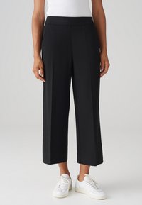 Pantalons larges noirs avec une texture lisse, dotés d'une taille haute et de plis sur le devant. Assortis à des baskets blanches.