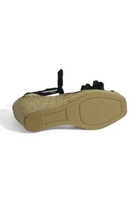 Schwarze Espadrille-Wedge mit einer Juteseilsohle, flachem Boden und zwei dekorativen Bindebändern an der Ferse. Mit einer strukturierten, glatten Oberfläche.