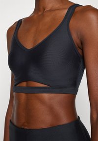 Sutiã desportivo preto sem costuras com decote em V e alças finas. Apresenta um detalhe recortado na cintura e ressaltos texturizados nas laterais.