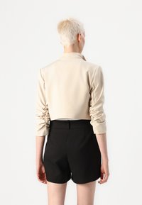 Beige lühikese lõikega jakk rullitud varrukatega, valmistatud siledast kangast. Kombineeritud kõrge pihaosaga mustade lühikestega, mis näitavad minimalistlikku disaini.