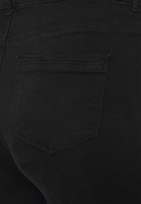 Jeans de denim preto com um bolso traseiro com uma costura discreta em forma de V. O tecido parece suave com um leve esticamento.