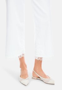 White cropped pants with a lace trim at the hem, paired with light beige mesh slingback flats featuring pointed toes and a low heel.