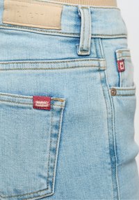 Vaqueros de mezclilla azul claro con un acabado texturizado, que presentan una etiqueta roja "BIG STAR" en el bolsillo trasero y un parche de cuero beige en la cintura.