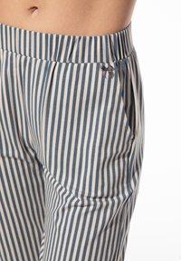 Taille en heupen van een persoon die blauwe en witte verticaal gestreepte broek draagt met een elastische tailleband en een klein grijs strikdetail nabij de zak.