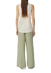 Ärmellose, hellbeige Bluse mit abgerundetem Saum, kombiniert mit lockeren, strukturierten, hellgrünen weit geschnittenen Hosen. Beide Teile sind glatt und atmungsaktiv.