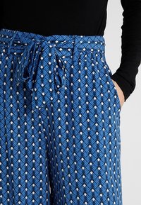 Blå mönstrade byxor med knytmidja, med en geometrisk bladdesign i vitt. Tillverkade av lätt material med sidofickor.