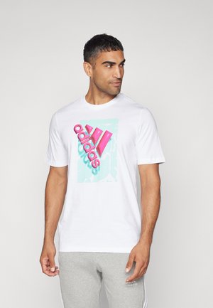 T-shirt bianca in cotone con un grande logo Adidas rosa su uno sfondo azzurro chiaro. Maniche corte e scollo rotondo.