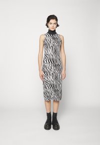 Abito senza maniche a stampa zebra in bianco e nero, con collo alto. Vestibilità sartoriale e lunghezza al ginocchio. Indossato con stivali alla caviglia neri con lacci.