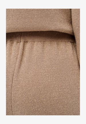 Gebreide trui in beige met subtiele gouden draad, voorzien van een geribde tailleband en een zachte textuur. Close-up gericht op de stofdetails.