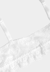 Bralette de encaje blanco con patrones florales, tirantes de satén ajustables y un borde de encaje con volantes en el borde inferior.