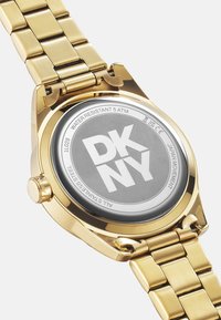 Gouden roestvrijstalen horloge met een gepolijste afwerking, met een ronde behuizing, grijze wijzerplaat en DKNY-logo. Waterbestendig tot 5 ATM.